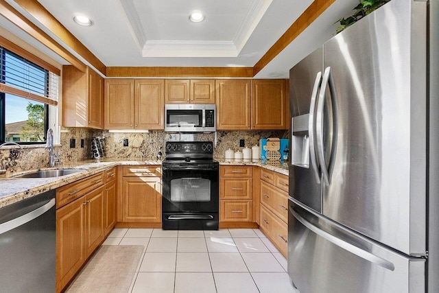 kitchen with a tray ceiling, light stone counters, light tile patterned floors, appliances with stainless steel finishes, and a sink