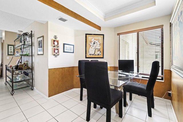 dining room featuring ornamental molding, wooden walls, light tile patterned flooring, wainscoting, and a raised ceiling