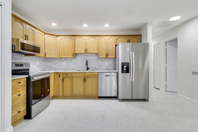 kitchen with stainless steel appliances, a sink, light countertops, light brown cabinetry, and tasteful backsplash