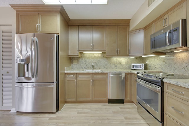 kitchen featuring light stone counters, light wood-style flooring, a sink, appliances with stainless steel finishes, and decorative backsplash