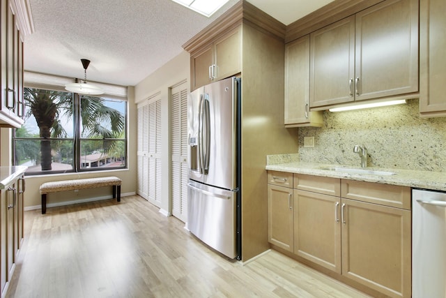 kitchen with a textured ceiling, stainless steel appliances, a sink, decorative backsplash, and light wood finished floors