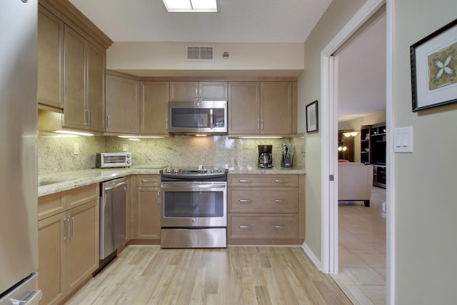 kitchen with stainless steel appliances, tasteful backsplash, visible vents, light wood-style flooring, and light stone countertops