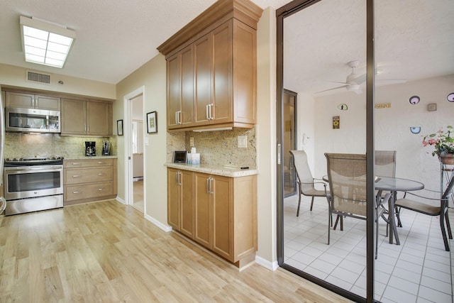 kitchen with light wood finished floors, stainless steel appliances, visible vents, decorative backsplash, and a ceiling fan