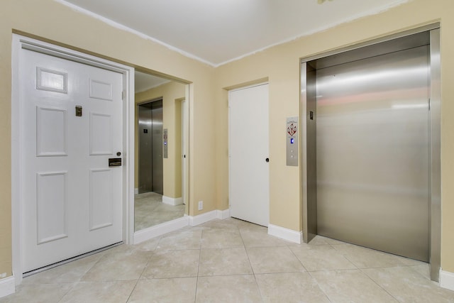 hallway featuring baseboards, light tile patterned flooring, and elevator