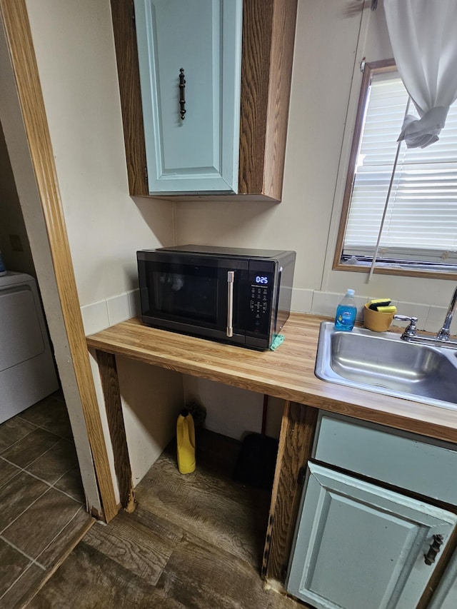 kitchen with butcher block countertops, black microwave, washer / clothes dryer, and a sink