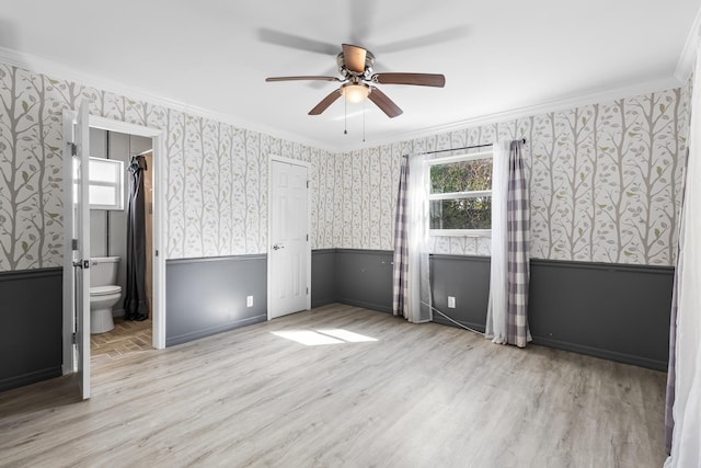 unfurnished bedroom with ornamental molding, ensuite bath, wood finished floors, wainscoting, and wallpapered walls