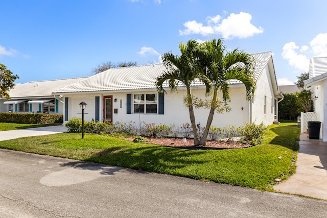 ranch-style house featuring a front yard, a tiled roof, driveway, and stucco siding