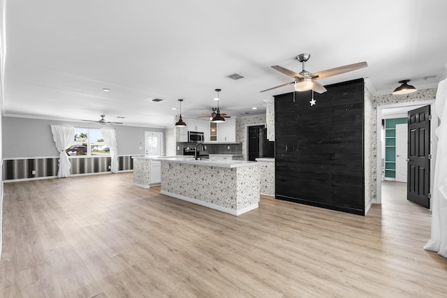 kitchen featuring light wood finished floors, stainless steel microwave, an island with sink, light countertops, and white cabinetry