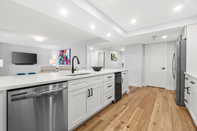 kitchen featuring stainless steel appliances, a sink, white cabinets, light wood-style floors, and light countertops