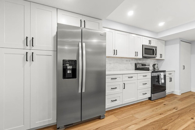 kitchen with light wood finished floors, light countertops, backsplash, appliances with stainless steel finishes, and white cabinetry