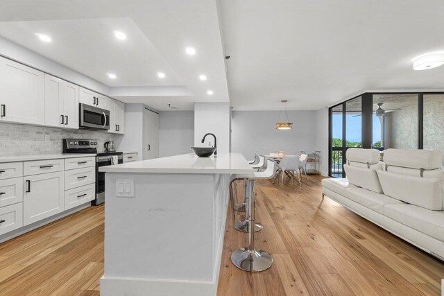 kitchen with stainless steel appliances, backsplash, light wood-style floors, open floor plan, and white cabinets