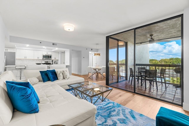 living room featuring visible vents, light wood-style floors, ceiling fan, a wall of windows, and baseboards