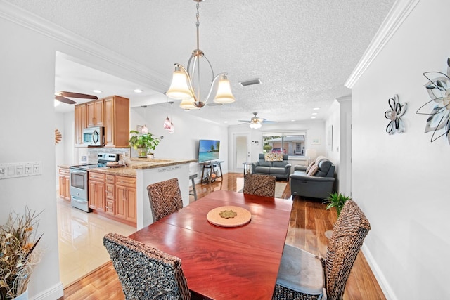 dining area with visible vents, ornamental molding, light wood-style flooring, ceiling fan with notable chandelier, and a textured ceiling