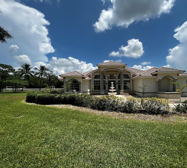 rear view of property featuring a tiled roof, a lawn, and stucco siding