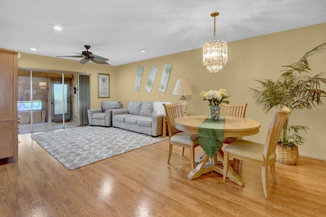 dining space with a textured ceiling, ceiling fan with notable chandelier, and light wood-style floors