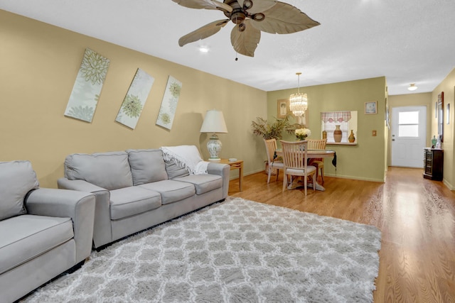 living room featuring ceiling fan with notable chandelier, baseboards, and wood finished floors