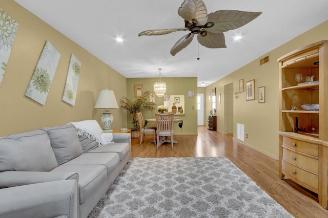 living area featuring ceiling fan with notable chandelier, light wood-type flooring, visible vents, and baseboards