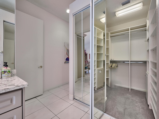 bathroom with tile patterned floors, a walk in closet, a textured ceiling, baseboards, and vanity