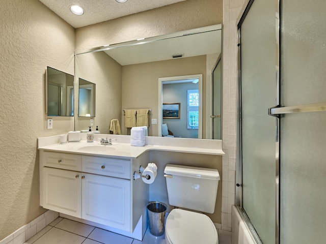 bathroom with tile patterned flooring, bath / shower combo with glass door, toilet, a textured wall, and vanity