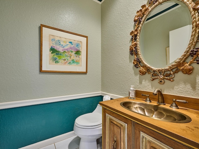 bathroom featuring toilet, vanity, and a textured wall