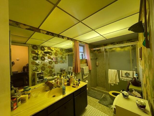 bathroom with a drop ceiling, tile patterned flooring, a shower stall, and vanity