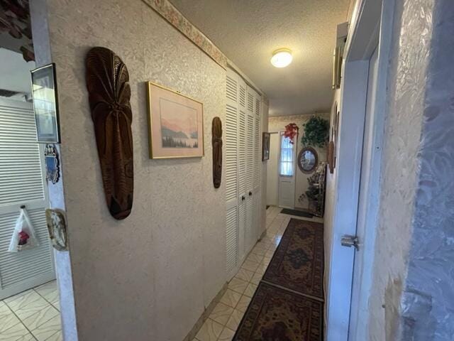 hallway featuring light tile patterned floors, a textured ceiling, and a textured wall