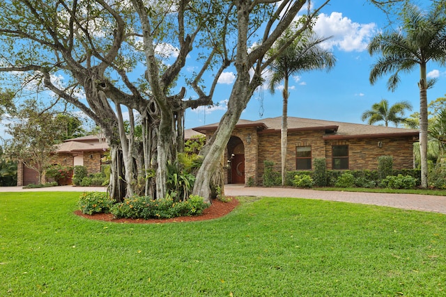 view of front of home featuring decorative driveway, stone siding, and a front yard