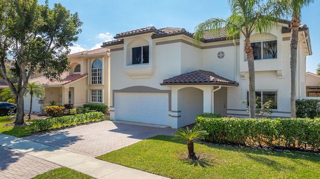 mediterranean / spanish home featuring a garage, a tile roof, decorative driveway, and stucco siding