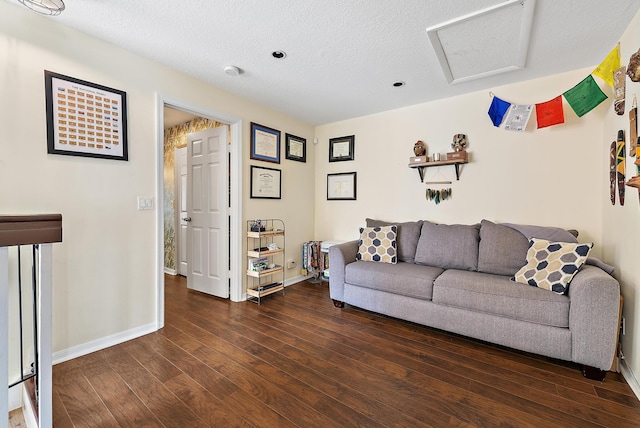 living area featuring a textured ceiling, wood-type flooring, attic access, and baseboards