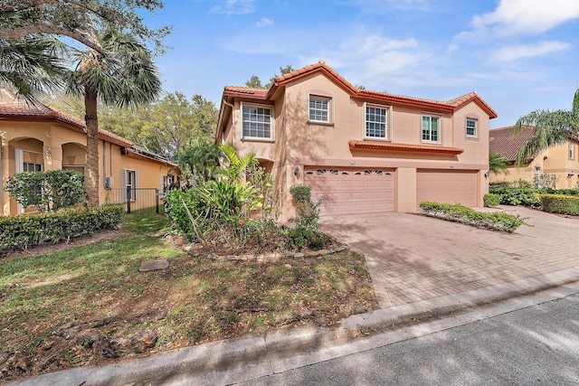 mediterranean / spanish-style house featuring an attached garage, a tile roof, decorative driveway, and stucco siding