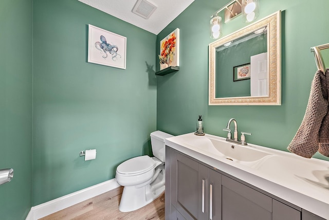 bathroom with visible vents, toilet, vanity, wood finished floors, and baseboards