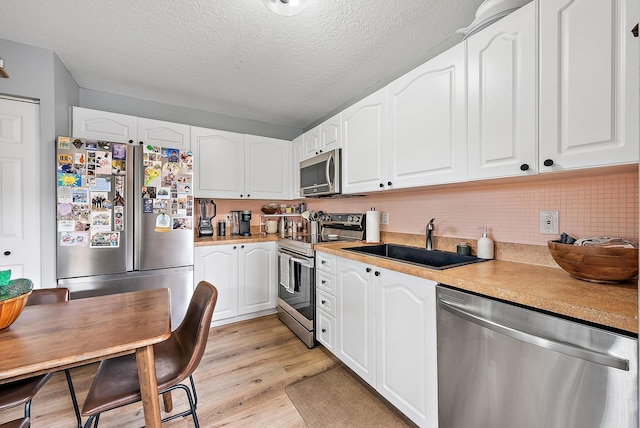 kitchen featuring light wood-style floors, appliances with stainless steel finishes, white cabinets, and a sink