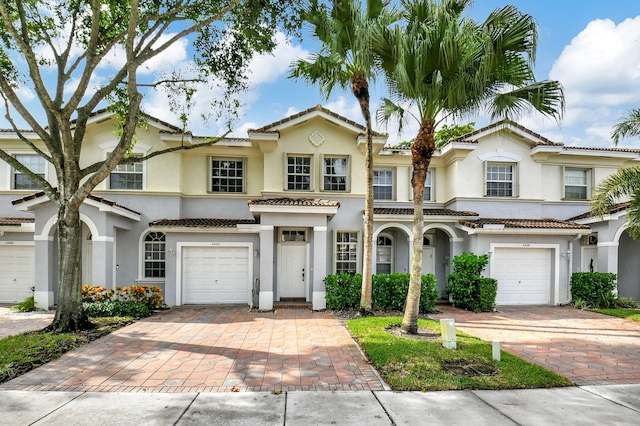 view of front of home with an attached garage, a tiled roof, decorative driveway, and stucco siding