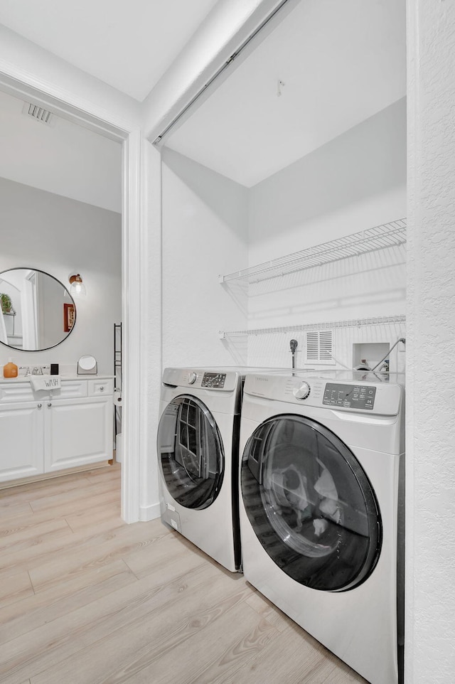 clothes washing area with light wood finished floors, separate washer and dryer, and visible vents