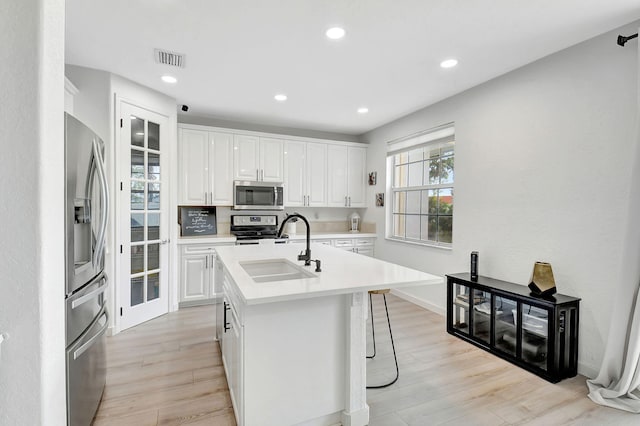 kitchen featuring stainless steel appliances, light countertops, white cabinetry, a sink, and light wood-type flooring