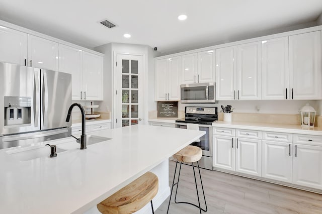 kitchen with visible vents, white cabinets, appliances with stainless steel finishes, a breakfast bar, and a sink