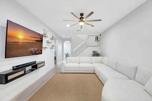 living area featuring arched walkways, wood finished floors, baseboards, stairway, and washer / dryer