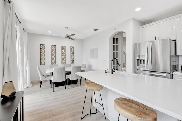 kitchen with arched walkways, light wood finished floors, white cabinets, a sink, and stainless steel fridge