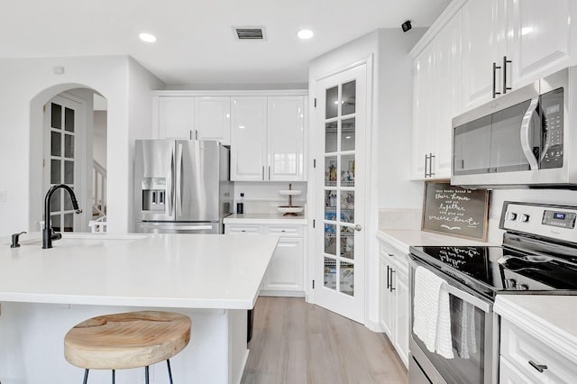 kitchen with stainless steel appliances, a sink, visible vents, white cabinets, and light wood-type flooring