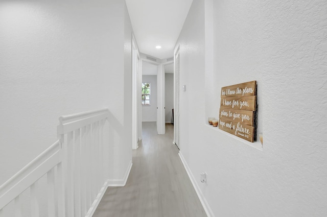 hallway featuring a textured wall, baseboards, wood finished floors, and an upstairs landing