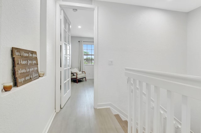 corridor featuring light wood-style floors, baseboards, and an upstairs landing