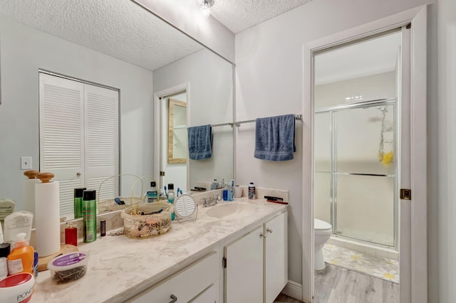 full bath featuring a stall shower, a textured ceiling, toilet, and vanity