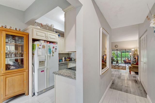 kitchen with white refrigerator with ice dispenser, light wood finished floors, light stone countertops, dishwasher, and baseboards