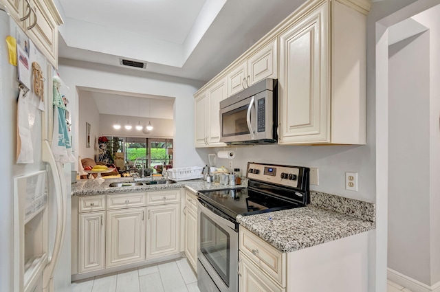 kitchen with light stone counters, stainless steel appliances, a sink, visible vents, and cream cabinetry