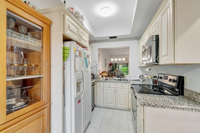 kitchen with stainless steel appliances, a sink, visible vents, light stone countertops, and a tray ceiling