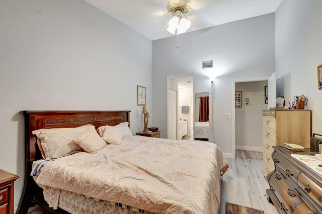 bedroom featuring visible vents, a towering ceiling, ensuite bathroom, light wood-style floors, and baseboards