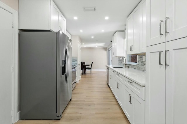 kitchen featuring stainless steel appliances, light countertops, light wood-style flooring, decorative backsplash, and a sink