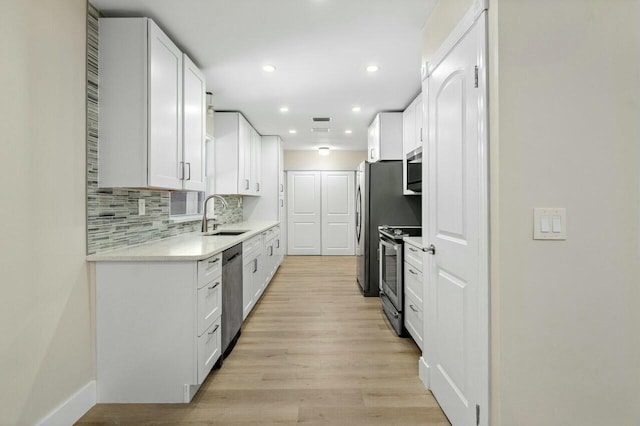 kitchen featuring decorative backsplash, light wood-style flooring, appliances with stainless steel finishes, white cabinetry, and a sink