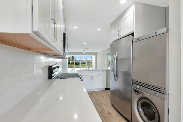 kitchen featuring stacked washer and clothes dryer, appliances with stainless steel finishes, light wood-style floors, white cabinets, and a sink