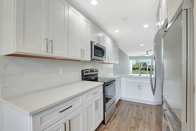 kitchen with appliances with stainless steel finishes, washer / clothes dryer, light wood-style floors, white cabinetry, and recessed lighting